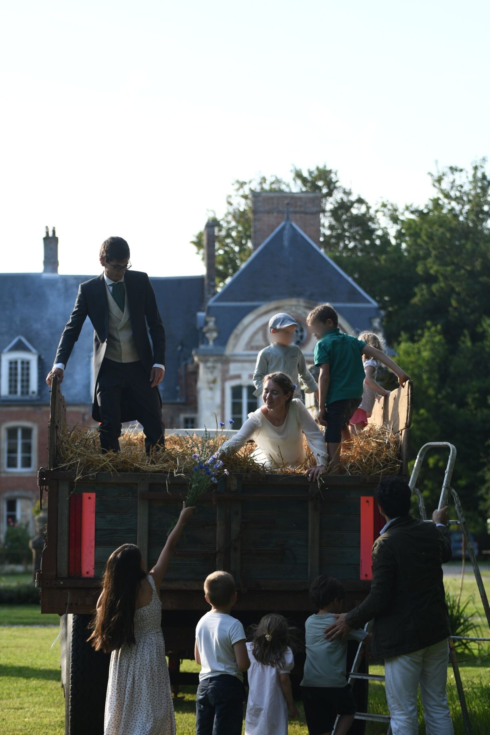 Enfants et mariés grimpant dans la remorque de paille devant le Château de Lihus
